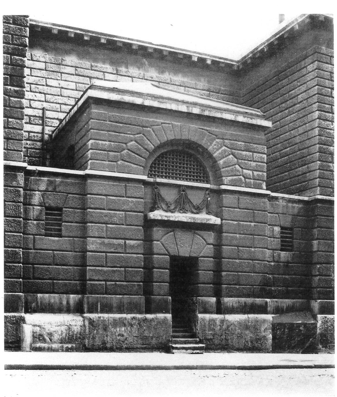 A black, stone built prison, with a narrow door below a high arch