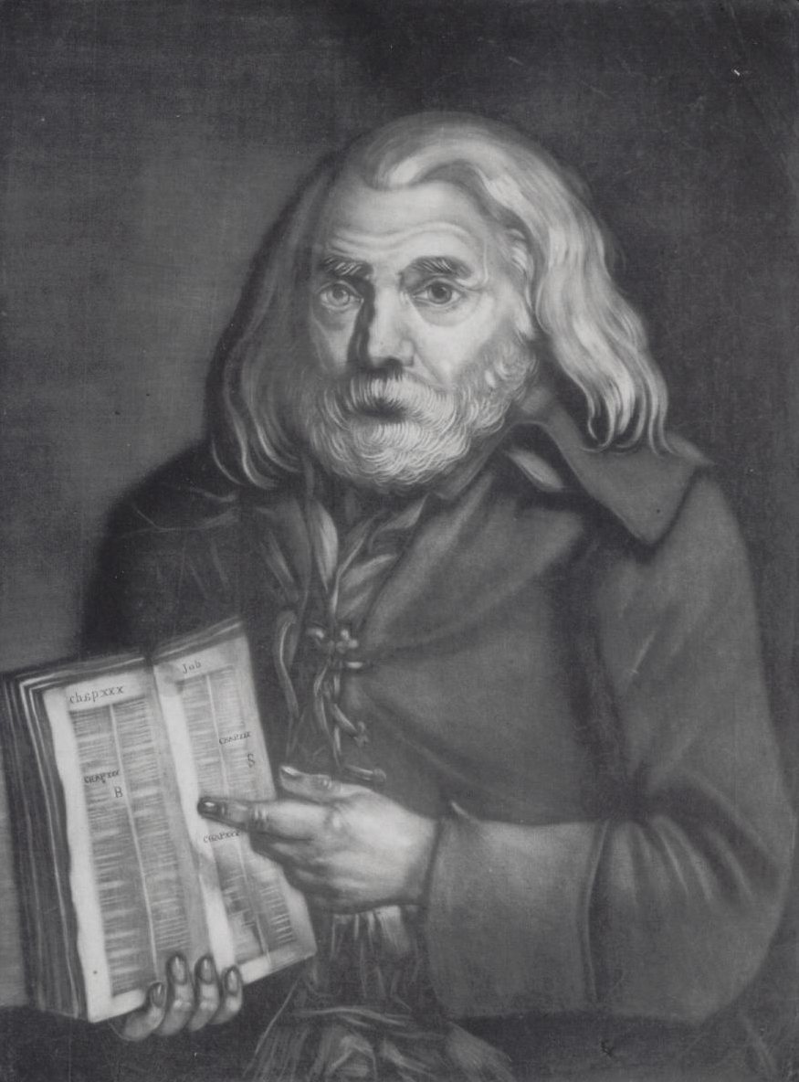 An older, white haired and bearded man in a ragged jacket points to an open copy of the Bible at the Book of Job